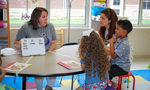 A teacher sits at a table with a student and the Tennessee Department of Education Commissioner